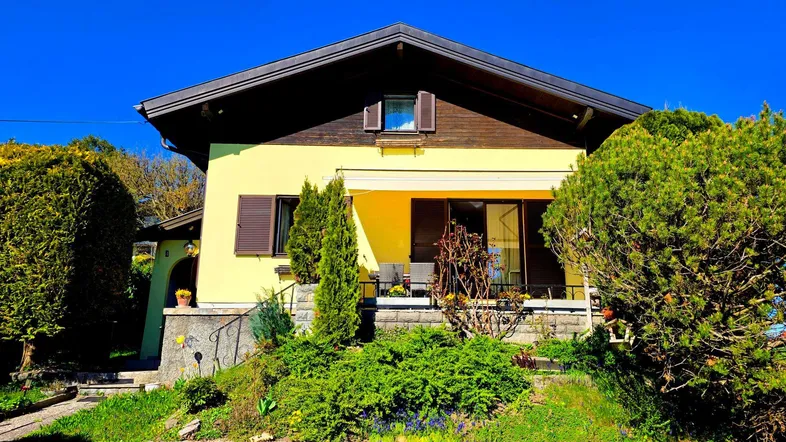Gelbes Einfamilienhaus mit dunklem Dach, umgeben von einem gepflegten Garten und einer möblierten Terrasse.