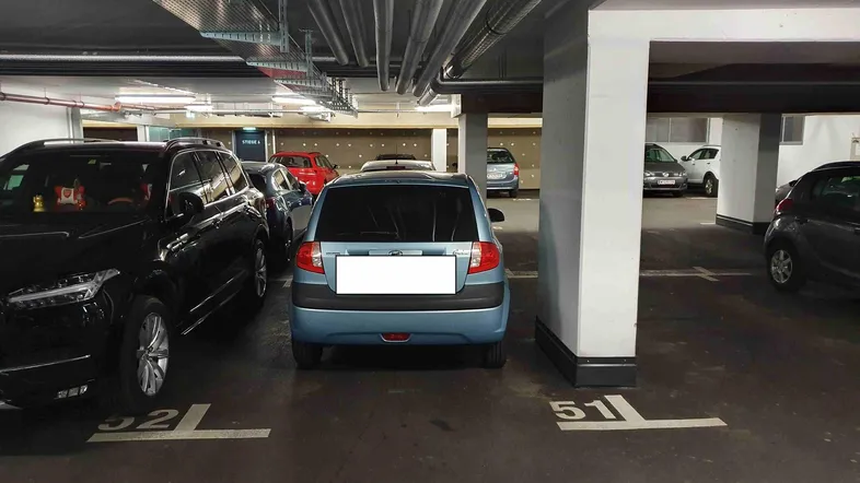 Tiefgarage mit mehreren geparkten Fahrzeugen und nummerierten Stellplätzen unter einer Betondecke.