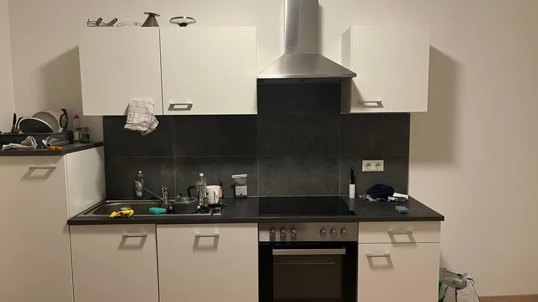 Moderne Einbauküche mit weißen Schränken, dunkler Arbeitsplatte und integrierten Geräten.
