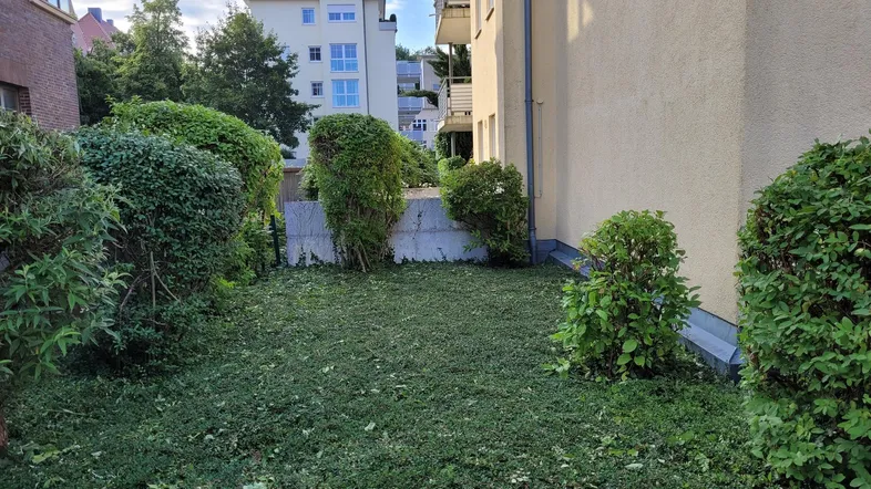 Gepflegter Gartenbereich mit Hecken und Blick auf umliegende Wohngebäude in städtischer Umgebung.