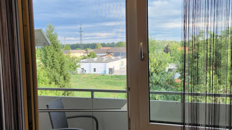 Kleiner Balkon mit einem Stuhl und Blick ins Grüne sowie auf die umliegende Landschaft.
