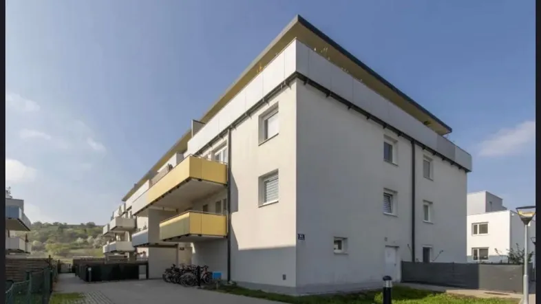 Modernes Mehrfamilienhaus mit weißer Fassade und gelben Balkonen unter blauem Himmel.