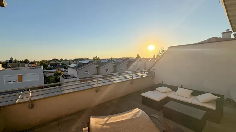 Sonnige Dachterrasse mit bequemen Loungemöbeln und weitem Blick über die Dächer bei Sonnenuntergang.