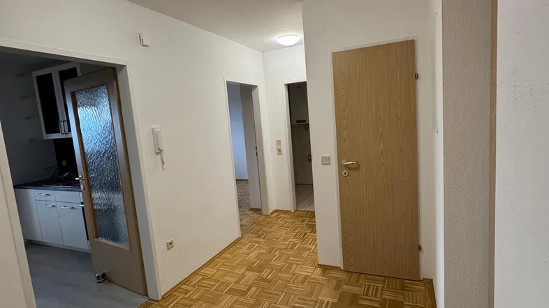 Heller Flur mit Parkettboden und Zugang zu verschiedenen Räumen, inklusive Blick in die Küche.