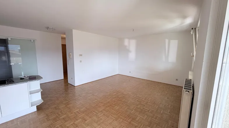 Helles Wohnzimmer mit Parkettboden und weiß gestrichenen Wänden, offen zur Küche.