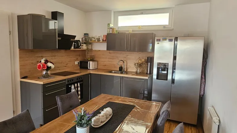Moderne Küche mit grauen Hochglanzfronten, Holzakzenten und integriertem Essbereich.
