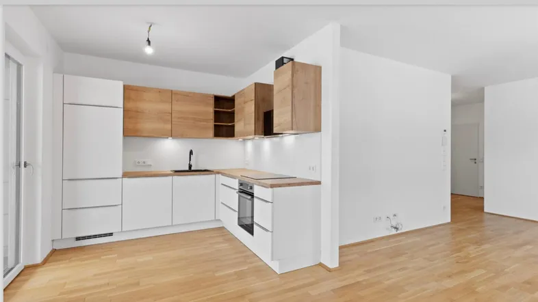 Moderne Einbauküche mit weißen und holzfarbenen Schränken, integriertem Backofen und hellem Parkettboden.
