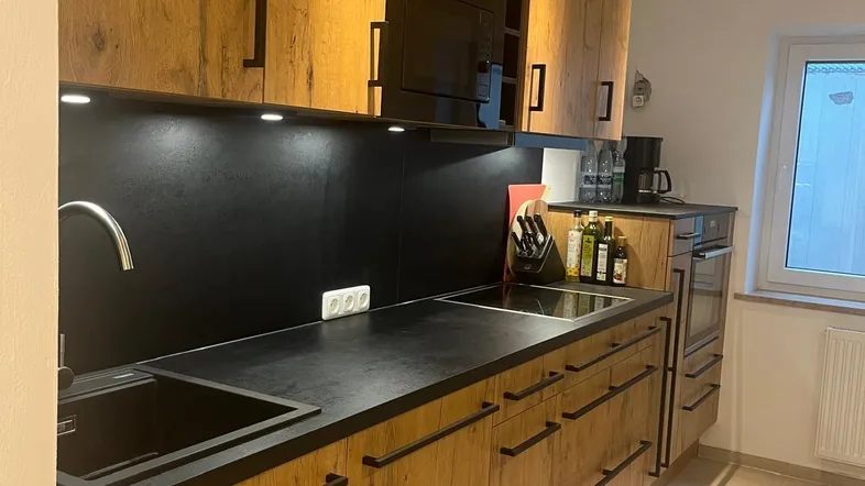 Moderne Küche mit Holzfronten, schwarzer Arbeitsplatte und integrierten Geräten.