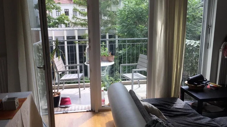 Helles Wohnzimmer mit Parkettboden und direktem Zugang zu einem möblierten Balkon mit Grünblick.
