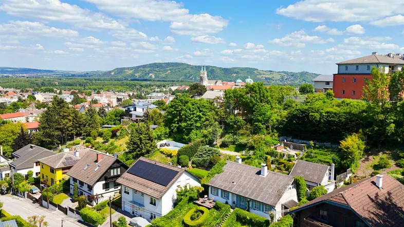 Luftaufnahme einer Wohnsiedlung mit Häusern, viel Grün und einem weiten Blick auf die Landschaft.