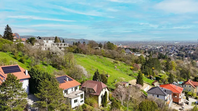 Luftaufnahme einer Wohnsiedlung am Hang mit grünen Hügeln und Fernblick auf die Stadt.