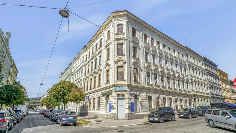 Historisches Eckgebäude in städtischer Umgebung mit klassischer Architektur und vielen Fenstern.