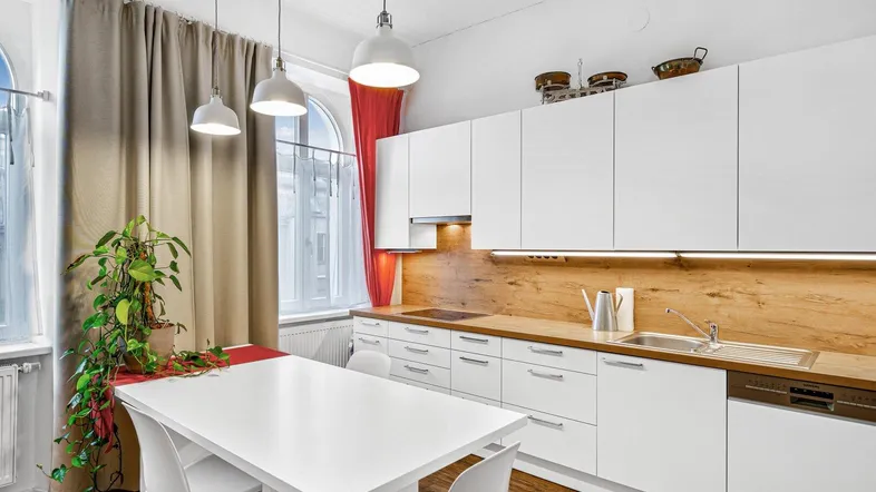Moderne Küche mit weißen Schränken, Holzarbeitsplatte und Essbereich am Fenster.