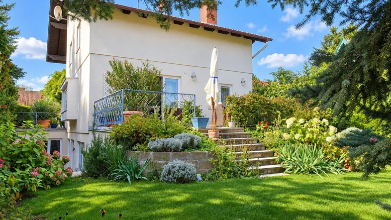 Gepflegter Gartenbereich mit Rasenfläche, Blumenbeeten und einer Steintreppe zum Haus.