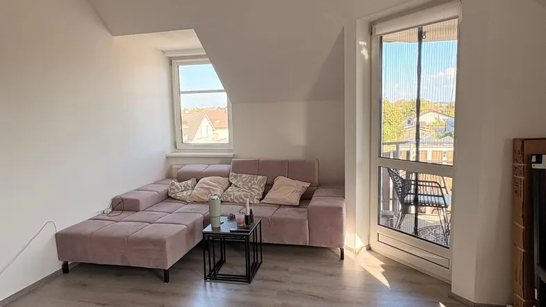 Helles Wohnzimmer mit gemütlichem Sofa, Laminatboden und Zugang zu einem Balkon.