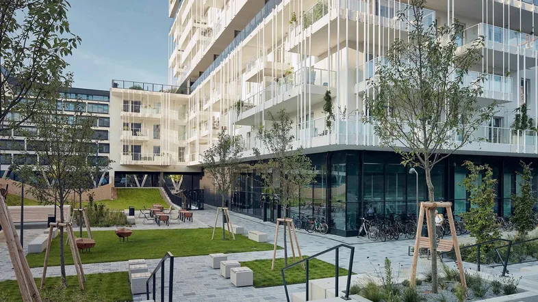 Moderner Apartmentkomplex mit begrüntem Innenhof und Sitzgelegenheiten im Freien.