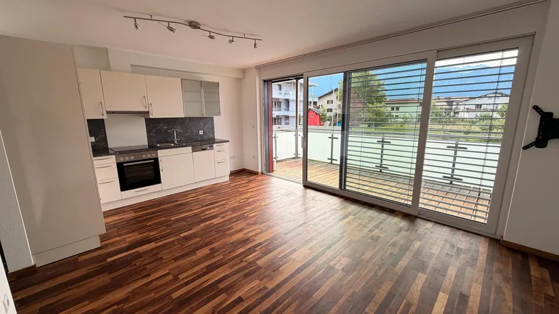 Offener Wohnbereich mit integrierter Küche, Holzboden und Zugang zum Balkon.