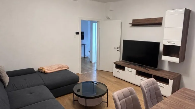 Moderner Wohn- und Essbereich mit dunklem Sofa, Esstisch und TV-Möbeln in hellem Ambiente.