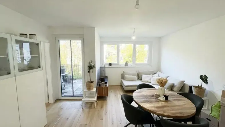 Heller Wohn- und Essbereich mit Holzboden, Zugang zum Balkon und großen Fenstern.