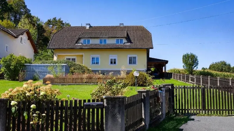 Traditionelles Einfamilienhaus mit gelber Fassade, Satteldach und gepflegtem Vorgarten.