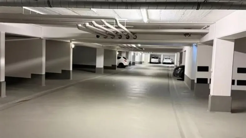 Helle Tiefgarage mit mehreren Stellplätzen, sauberem Betonboden und sichtbaren Leitungen an der Decke.