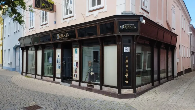 Außenansicht eines Eckgebäudes mit großen Schaufenstern und Geschäftsfassade an einer belebten Straße.