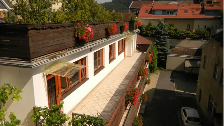 Langer Balkon mit Blumenkästen und Blick auf die umliegenden Gebäude und grüne Hügel.
