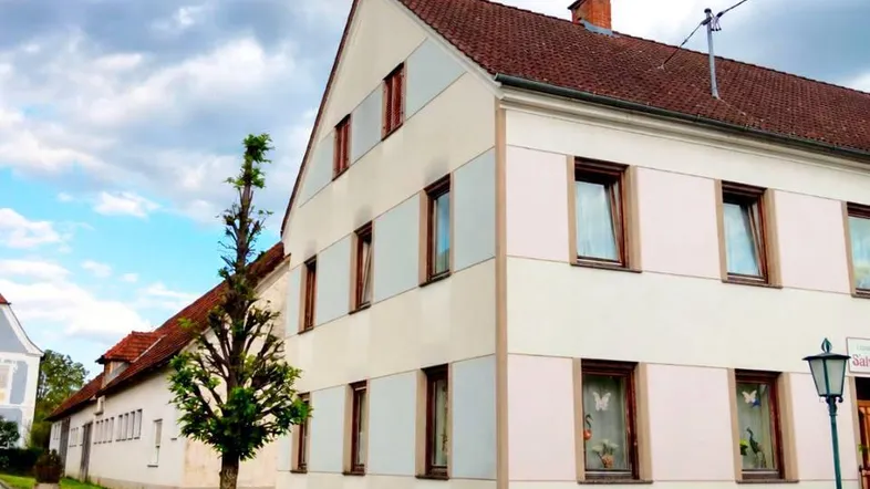 Seitenansicht eines traditionellen Wohnhauses mit heller Fassade und Satteldach unter bewölktem Himmel.