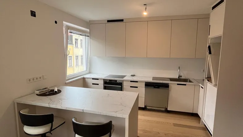 Moderne Küche mit heller Arbeitsplatte, Kücheninsel und Holzboden, ideal für geselliges Kochen.