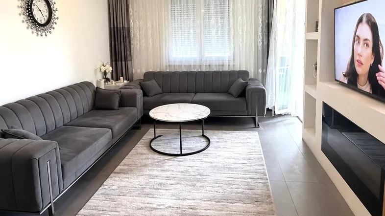 Modernes Wohnzimmer mit bequemen grauen Sofas, einem Couchtisch und einem Fernseher an der Wand.