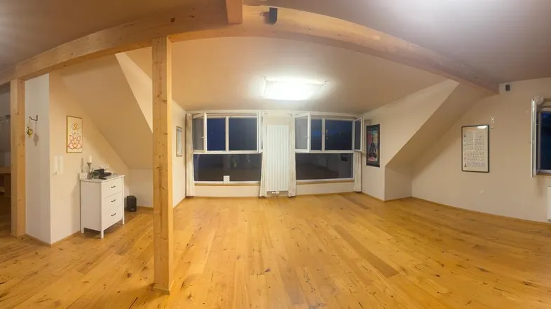 Geräumiger Wohnbereich im Dachgeschoss mit Holzbalken, Holzboden und mehreren Fenstern.