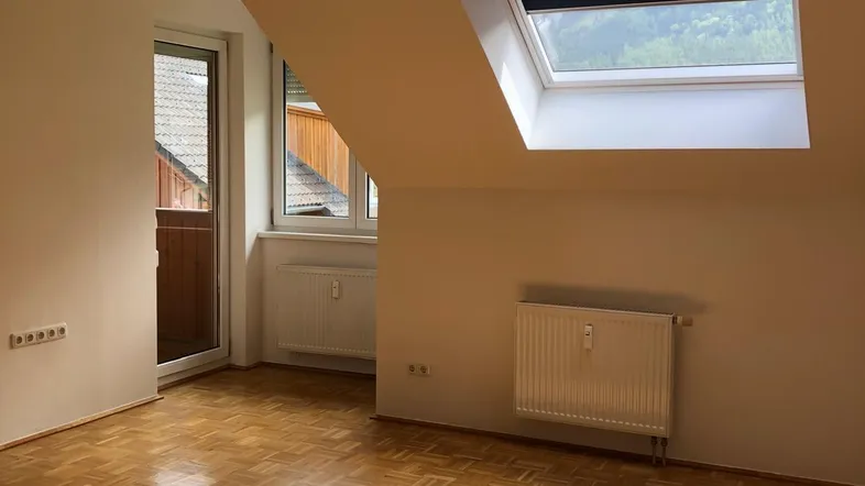 Helles Zimmer im Dachgeschoss mit Parkettboden, Dachfenster und Zugang zum Balkon.