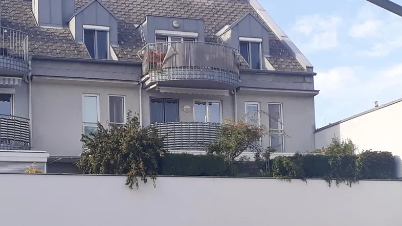 Fassade eines Mehrfamilienhauses mit einem runden Balkon und Dachgauben unter blauem Himmel.
