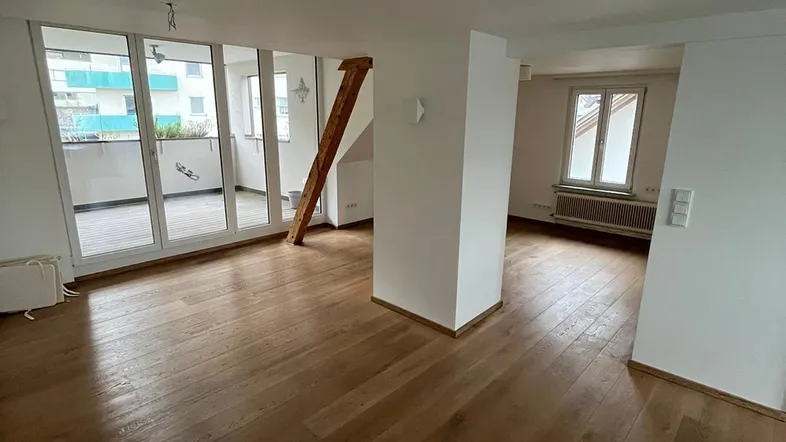 Helles Wohnzimmer mit Holzboden, weißen Wänden und Zugang zu einem Balkon.