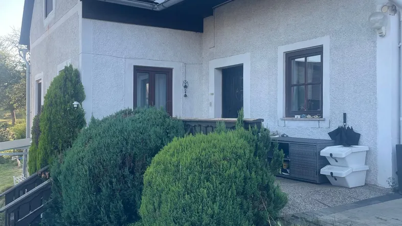 Traditionelles Haus mit weißer Fassade, dunklem Dach und gepflegten Büschen im Vorgarten.