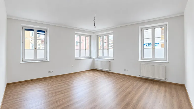 Helles, leeres Zimmer mit Laminatboden und mehreren Fenstern, bereit zur individuellen Gestaltung.