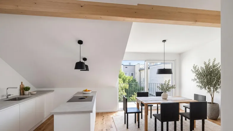 Moderne offene Wohnküche mit Essbereich, Holzbalken und Zugang zu einem Balkon.