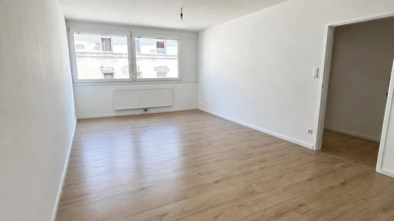 Helles, leeres Zimmer mit neuem Laminatboden und Blick auf die umliegenden Gebäude.