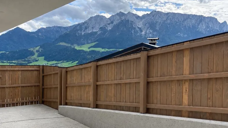 Betonierter Außenbereich mit Holzzaun und beeindruckendem Bergblick unter bewölktem Himmel.