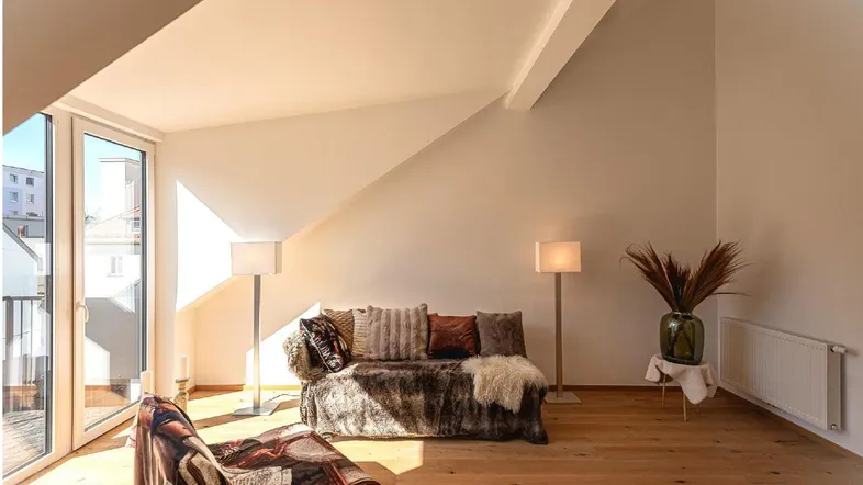 Helles Wohnzimmer mit gemütlichem Sofa, Holzboden und Zugang zu einem Balkon unter der Dachschräge.