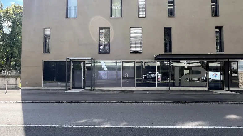 Moderne Gebäudefassade mit großen Schaufenstern und Eingangsbereich an einer Straße.