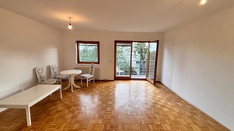 Helles Wohnzimmer mit Parkettboden, Zugang zum Balkon und Blick ins Grüne.