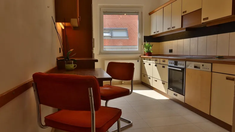 Helle Küche mit Einbauschränken, integriertem Backofen und einem kleinen Essbereich am Fenster.