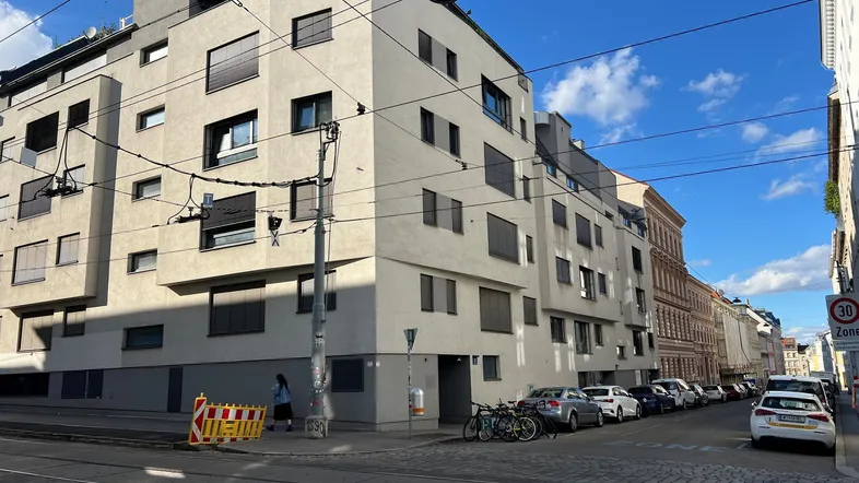Moderne Wohngebäude-Fassade an einer städtischen Straße mit parkenden Autos und blauem Himmel.