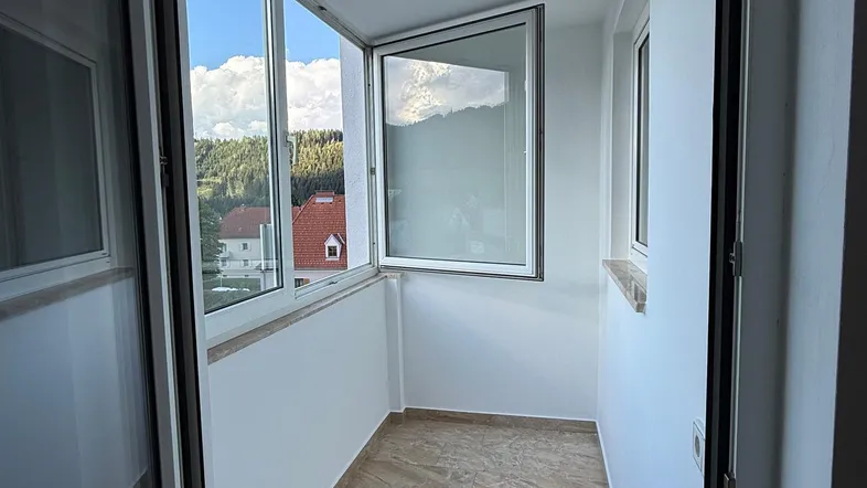 Heller, verglaster Balkon mit Fliesenboden und weitem Blick auf die umliegende Landschaft.
