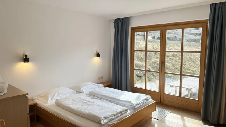 Helles Schlafzimmer mit Holzboden, Doppelbett und Zugang zu einer Terrasse mit Blick auf die Landschaft.