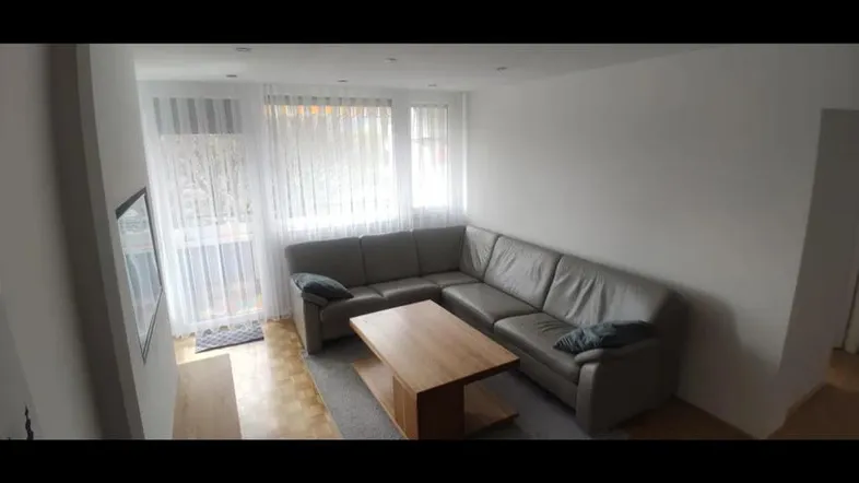 Helles Wohnzimmer mit großem Ecksofa, Couchtisch und Fenstern mit Vorhängen.