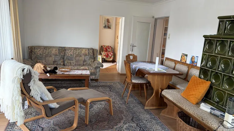 Gemütlicher Wohn- und Essbereich mit traditionellem Kachelofen, Sofa und Esstisch.