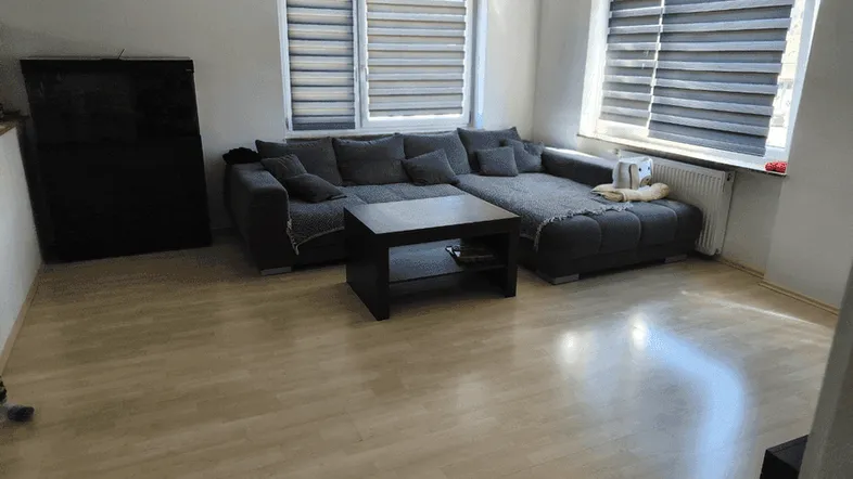 Helles Wohnzimmer mit großem Ecksofa, Couchtisch und hellem Laminatboden, gut beleuchtet durch Fenster.