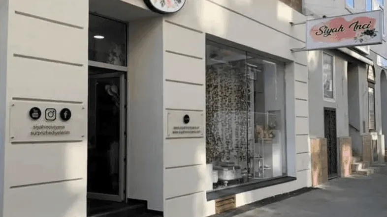 Außenansicht eines Geschäftsgebäudes mit Schaufenster und Eingangsbereich, die Fassade ist hell gestrichen.